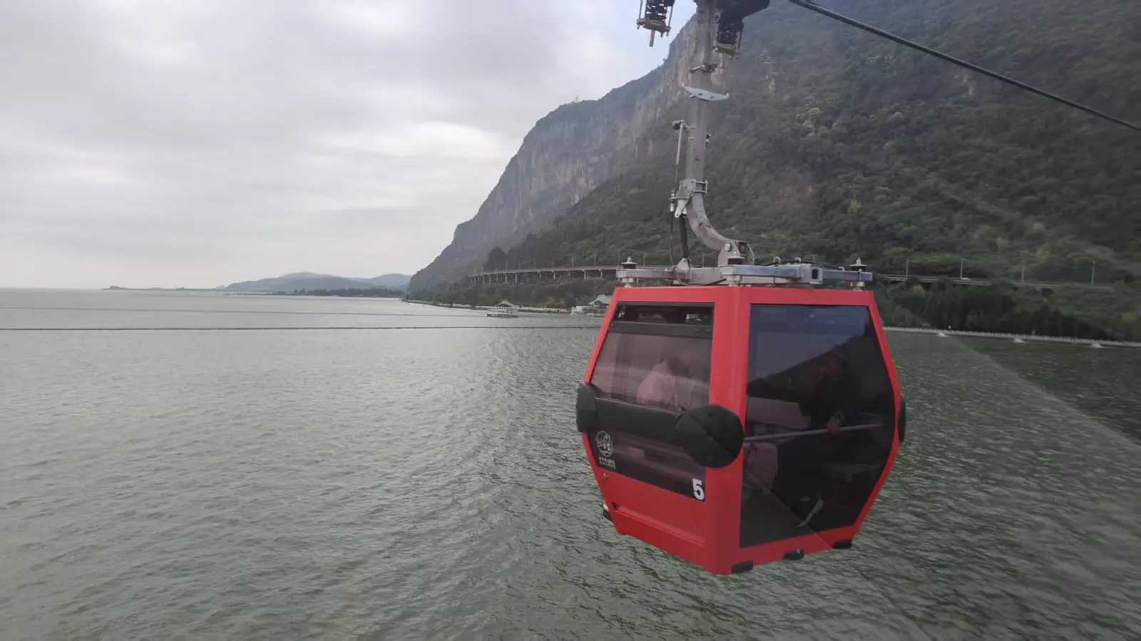 A red cable car travelling above water beside a mountain